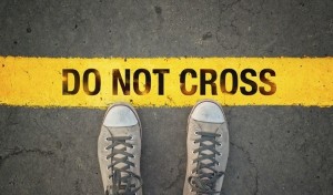 Man in sneakers standing at the yellow line with Do Not cross message